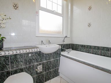 A bathroom with a bathtub sink toilet and decorated tiled walls at Weymouth Bay Apartment A in Weymouth