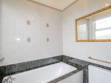 A bathroom with a bathtub tiled walls a gold framed mirror window radiator and a towel rail at Weymouth Bay Apartment A Weymouth