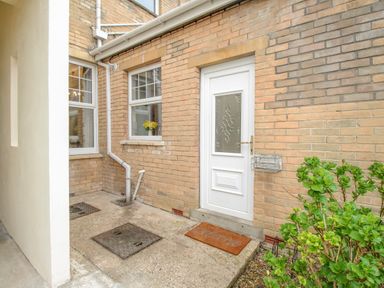 A brick exterior with a white door and windows a welcome mat and a green bush at Weymouth Bay Apartment A Weymouth