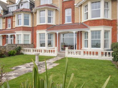 A front view of a brick house with white framed windows and a small stone pathway on a lawn at Weymouth Bay Apartment A in Weymouth