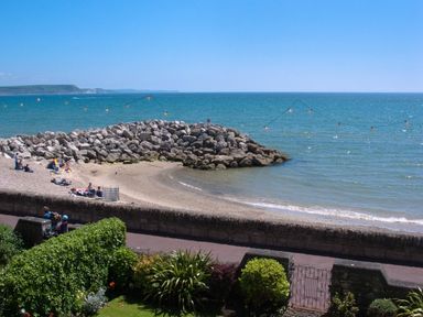 A beach with people sitting on the sand and rocks by the sea at Weymouth Bay Apartment A in Weymouth