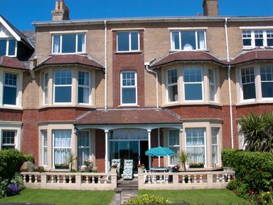 A brick house with bay windows a small patio and garden with flowers at Weymouth Bay Apartment A Weymouth