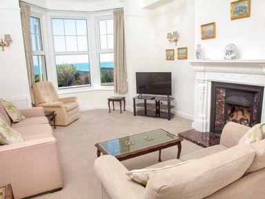 A living room with sofas an armchair a glass coffee table a television and a fireplace with paintings on the wall at Weymouth Bay Apartment A Weymouth