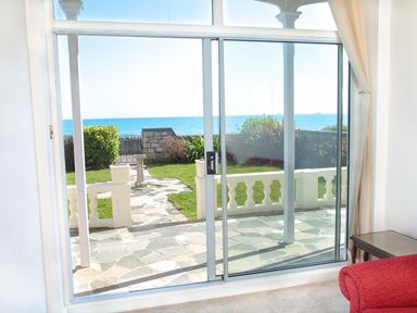A glass sliding door opening to a patio with a stone path and green lawn overlooking the sea at Weymouth Bay Apartment A in Weymouth