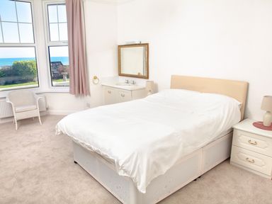 A bedroom with a double bed two bedside tables a chair and a window showing the sea at Weymouth Bay Apartment A in Weymouth