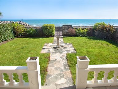 A garden with a stone pathway, grass, plants, and a view of the sea at Weymouth Bay Apartment A in Weymouth