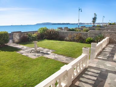 A garden with a stone pathway and sundial facing the sea at Weymouth Bay Apartment A in Weymouth