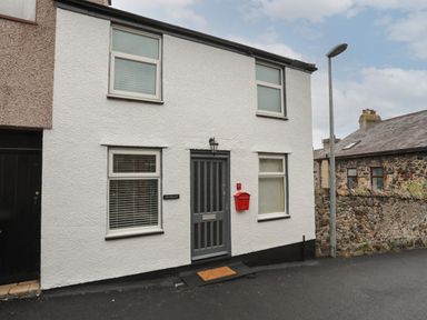 A white two-story house with four windows a gray door and a red mailbox on a street at Clydfan in Caernarfon