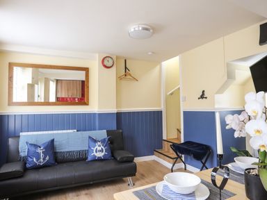 A living room with a black sofa blue cushions and a staircase at Clydfan in Caernarfon