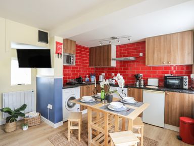 A kitchen with wooden cabinets red tiled backsplash dining table with chairs and a wall mounted television at Clydfan in Caernarfon