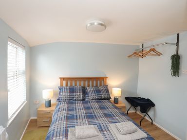 A bedroom with a double bed chest of drawers two lamps a window and a hanging rack with hangers and a plant at Clydfan in Caernarfon