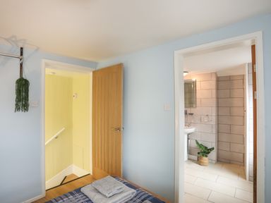 A bedroom view showing a doorway to a stairwell with yellow walls and an open door leading to a tiled bathroom with a plant on the floor at Clydfan in Caernarfon