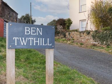 A road with a sign that reads Ben Twthill next to grass and a stone wall with a house behind it at Clydfan in Caernarfon
