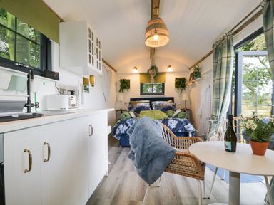 A small living space with a bed at the end a kitchen area on the left and a small round table with chairs on the right at High Rigg Shepherd's Sunset in Brampton Cumbria