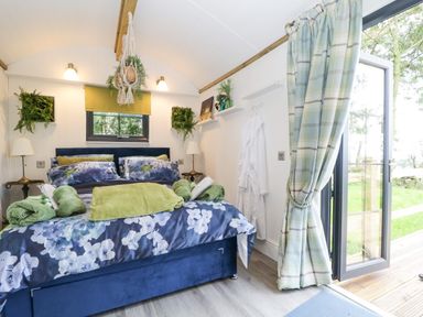 A bedroom with a blue floral bedspread green towels and robes hanging by the door at High Rigg Shepherd's Sunset in Brampton Cumbria