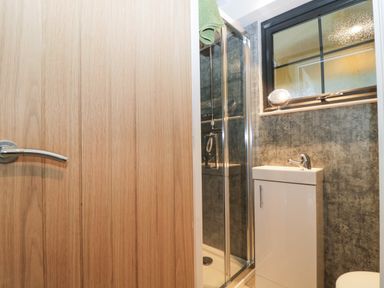 A bathroom with a wooden door shower cubicle a white sink unit and a window with a mirror on the sill at High Rigg Shepherd's Sunset in Brampton Cumbria