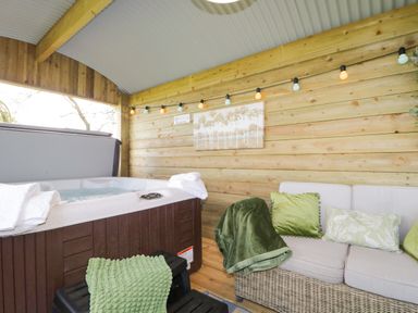 An outdoor covered area with a hot tub towels a wicker sofa with cushions and a blanket at High Rigg Shepherd's Sunset in Brampton Cumbria