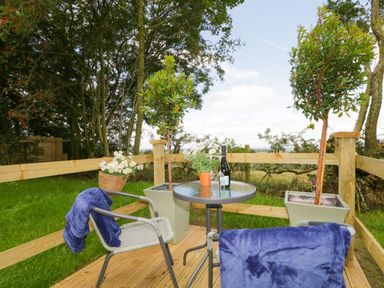 A small outdoor deck with a round glass table two chairs with blue blankets and potted plants at High Rigg Shepherds Sunset in Brampton Cumbria