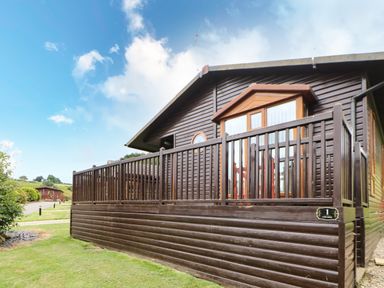 A wooden cabin with a fenced porch in a grassy area at Badgers Retreat in Tunstall near Hipswell