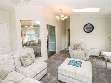 A living room with two armchairs and a sofa with cushions a square ottoman with a board game and a clock on the wall at Badgers Retreat in Tunstall near Hipswell