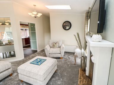 A living room with armchairs ottoman and a wall-mounted television at Badgers Retreat in Tunstall near Hipswell