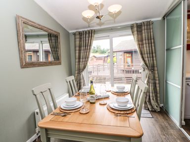 A dining room with table set for four and sliding glass door with curtains at Badgers Retreat in Tunstall near Hipswell