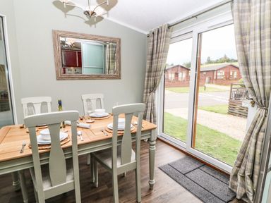 A dining area with a wooden table set for four by sliding glass doors with plaid curtains at Badgers Retreat in Tunstall near Hipswell