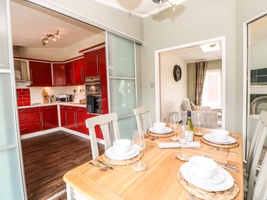 A dining area with a wooden table set with white dishes and glasses next to a kitchen with red cabinets at Badgers Retreat in Tunstall near Hipswell