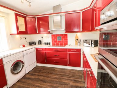 A kitchen with red cabinets white countertops washing machine dishwasher oven microwave toaster and kettle at Badgers Retreat in Tunstall near Hipswell