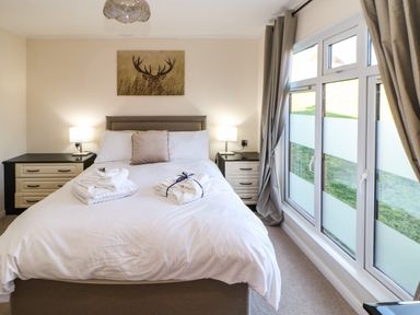 A bedroom with a bed between two bedside tables and a window with curtains at Badgers Retreat Tunstall near Hipswell