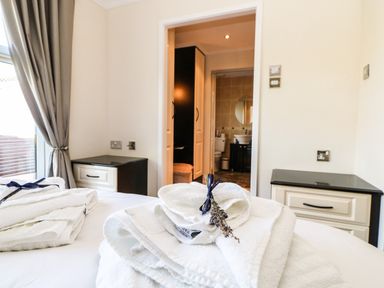 A bedroom with folded white towels on the bed a window with curtains and a view into a bathroom at Badgers Retreat in Tunstall near Hipswell