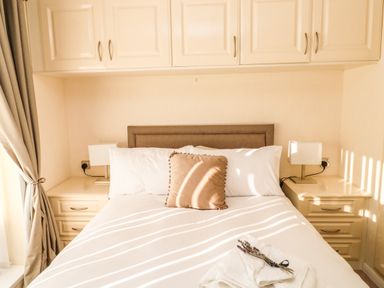 A bedroom with a bed and bedside tables with lamps and overhead cabinets at Badgers Retreat in Tunstall near Hipswell