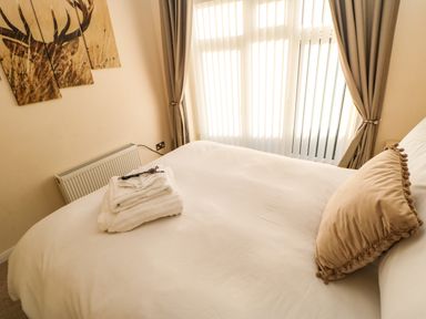 A bedroom with a bed with white bedding a beige pillow folded towels on the bed and a large window with curtains at Badgers Retreat in Tunstall near Hipswell