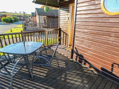 A wooden patio with metal table and chairs outside a cabin at Badgers Retreat in Tunstall near Hipswell