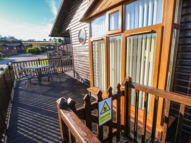 A wooden deck with table and chairs outside wooden cabins at Badgers Retreat in Tunstall near Hipswell