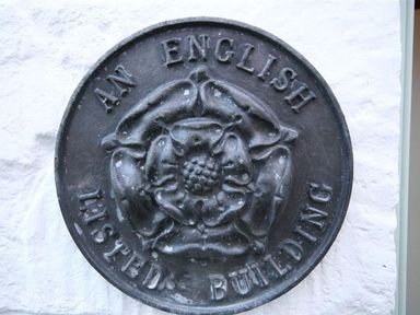 A circular metal plaque with a rose design and the words an english listed building mounted on a white wall