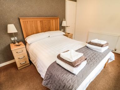 A bedroom with a double bed with white linens and folded towels on a quilted runner at Hillside View in Alnwick