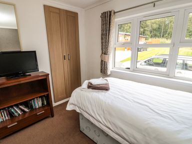 A bedroom with a single bed folded towels on it a window with curtains a wooden cabinet with a television and books at Hillside View in Alnwick