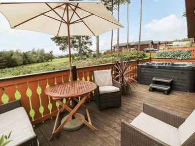 A wooden deck with patio furniture umbrella and a hot tub overlooking greenery at Hillside View in Alnwick