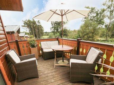 A balcony with wicker chairs a round wooden table and an umbrella at Hillside View in Alnwick