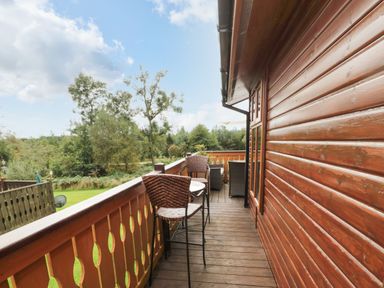 A wooden balcony with outdoor chairs and table overlooking trees and grass at Hillside View in Alnwick