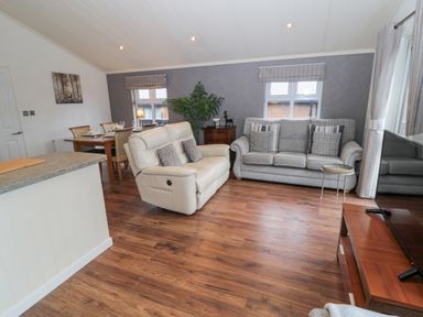 A living area with two sofas a wooden dining table and chairs a television on a wooden stand and windows at Hillside View in Alnwick
