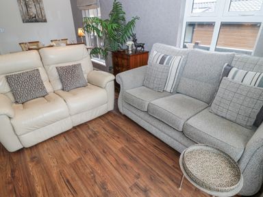 A living room with two sofas a small round table a wooden chest with decorations and dining table in the background at Hillside View in Alnwick