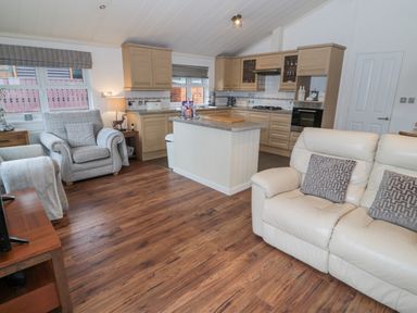 An open plan living room and kitchen with wooden cabinets and a white leather sofa at Hillside View in Alnwick