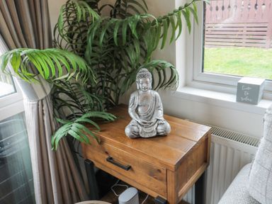 A wooden side table with a Buddha statue and a potted plant near a window with a sign on the sill at Hillside View in Alnwick
