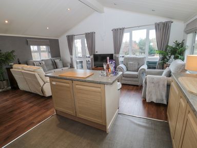 A living area with grey sofas a TV and wooden kitchen island at Hillside View in Alnwick