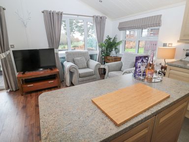 A living area with two armchairs a television on a wooden stand and a kitchen counter with a cutting board at Hillside View in Alnwick