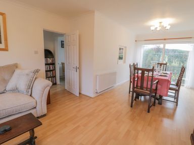 A dining room with a table and chairs near a sliding glass door and a living room with a sofa and pillows at Sea Change in Newholm near Whitby