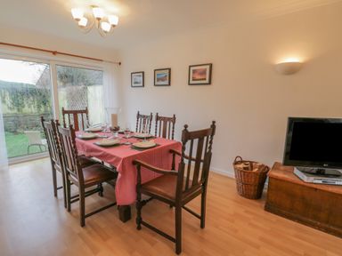 A dining room with a table set for six and a television on a wooden cabinet at Sea Change in Newholm near Whitby
