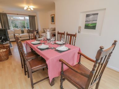 A dining area with wooden chairs and a table set with a red tablecloth and glassware next to a living room with sofas in Sea Change Newholm near Whitby